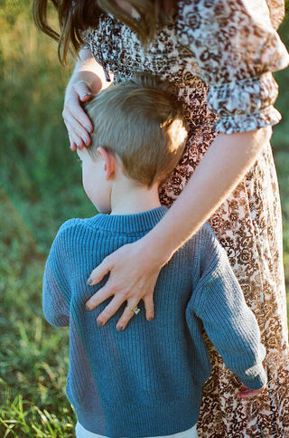 a mom places her hand gently on her son's back during a sunrise family session at mcintire park in charlottesville virginia