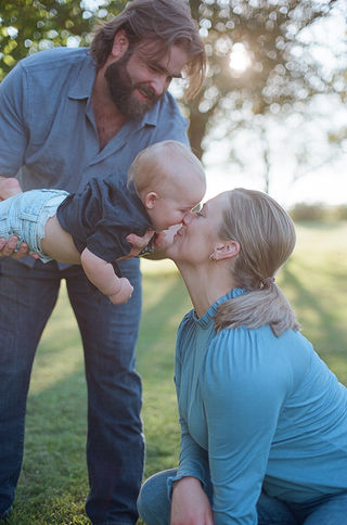 a dad bringing his son over for a kiss from mom during a sunset family photographer session with charlottesville photographer Laura Richards