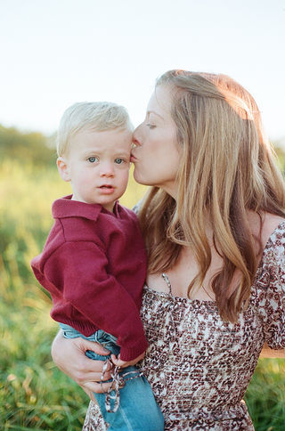 mom kissing her toddler son during a sunrise family photo session at mcintire park in charlottesville virginia