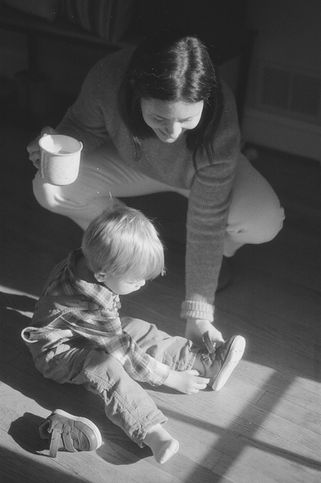 a mom helps her young son put on his shoes during an at-home family photo session in charlottesville virginia