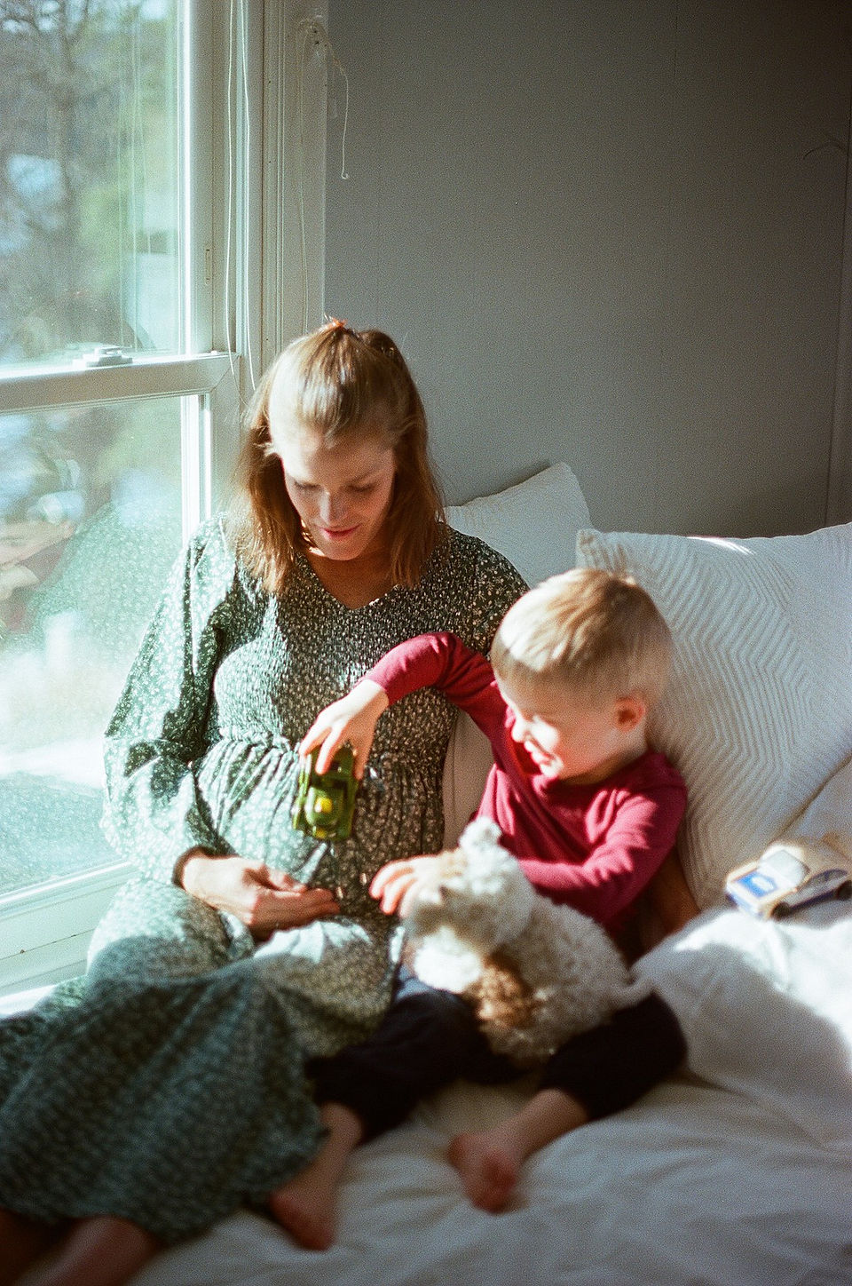 mom sits next to her young son while he runs a toy car over her pregnant belly