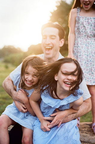 a dad and his daughters laughing during a golden-hour family photography sessio at mcintire park in charlottesville virginia