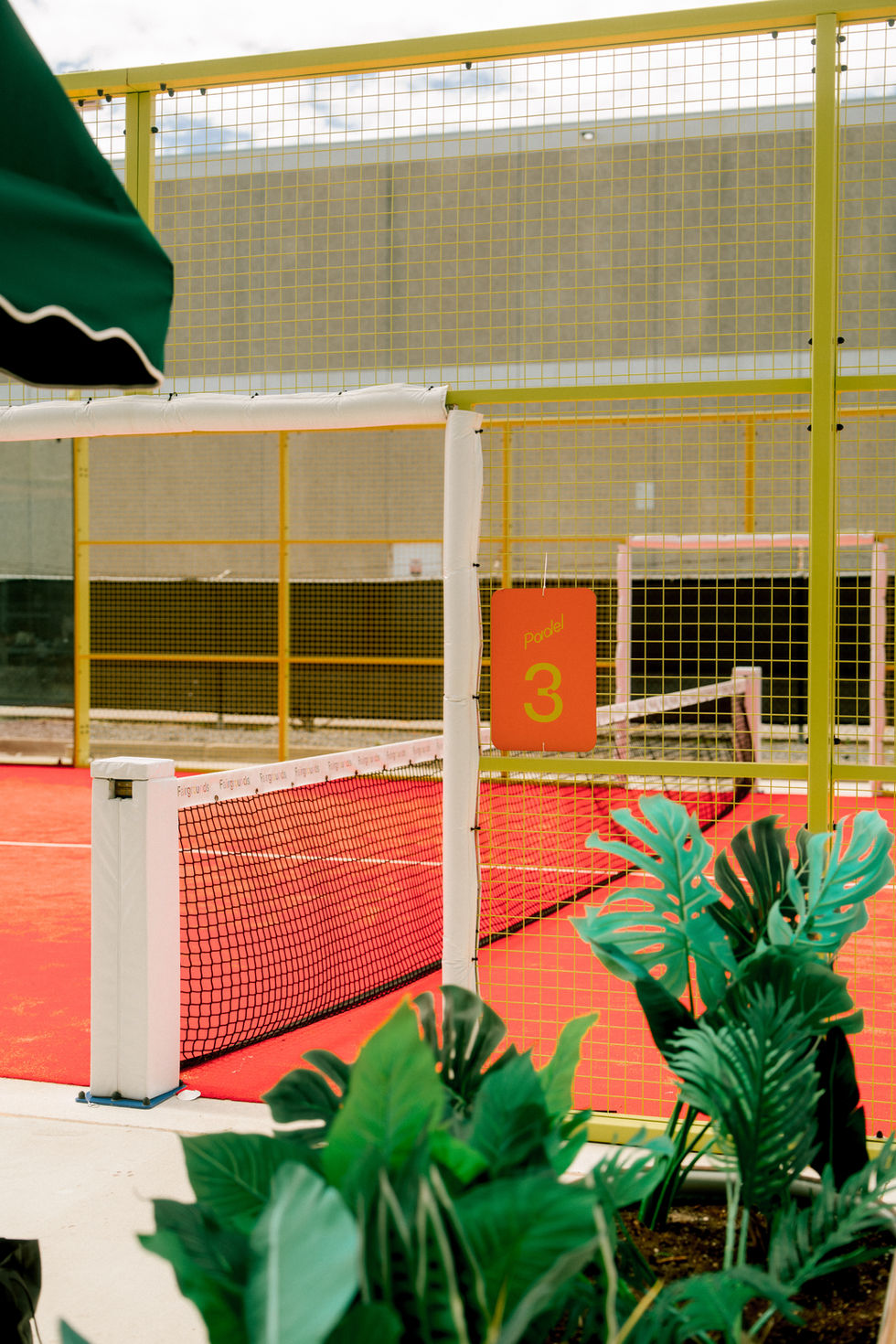 Indoor tennis court with red surface and green plants.