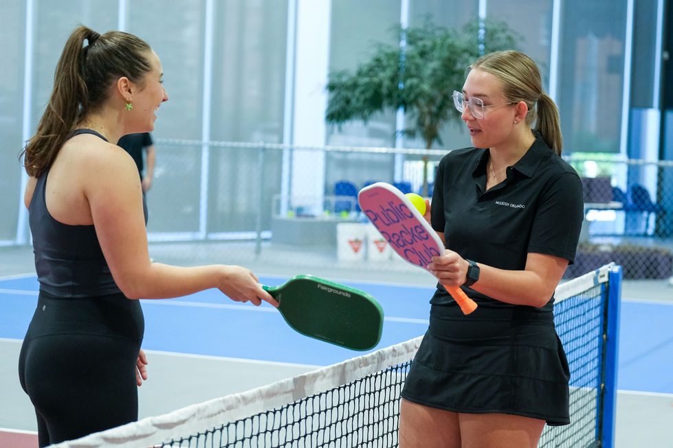 Two people playing pickleball indoors, holding paddles.