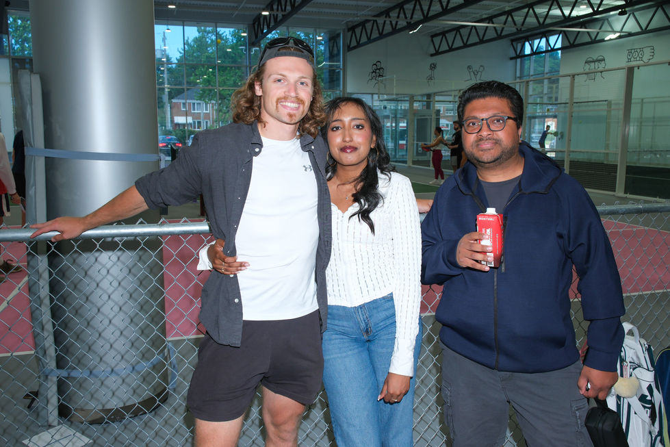 Three people posing together, one holding a drink.