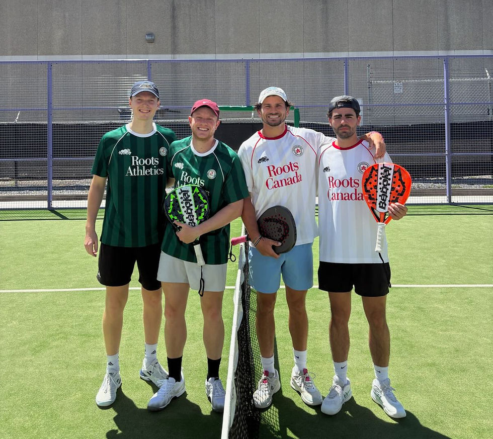 Four men pose on a pickleball court with paddles, wearing Roots Athletics and Roots Canada jerseys, smiling in bright sun
