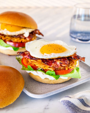 Burger breakfast avec œuf au plat, bacon croustillant et pain brioché, photographie food en lumière naturelle.