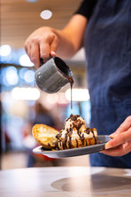 Main qui verse du coulis de chocolat chaud sur le dessert de choux et boule de glace vanille