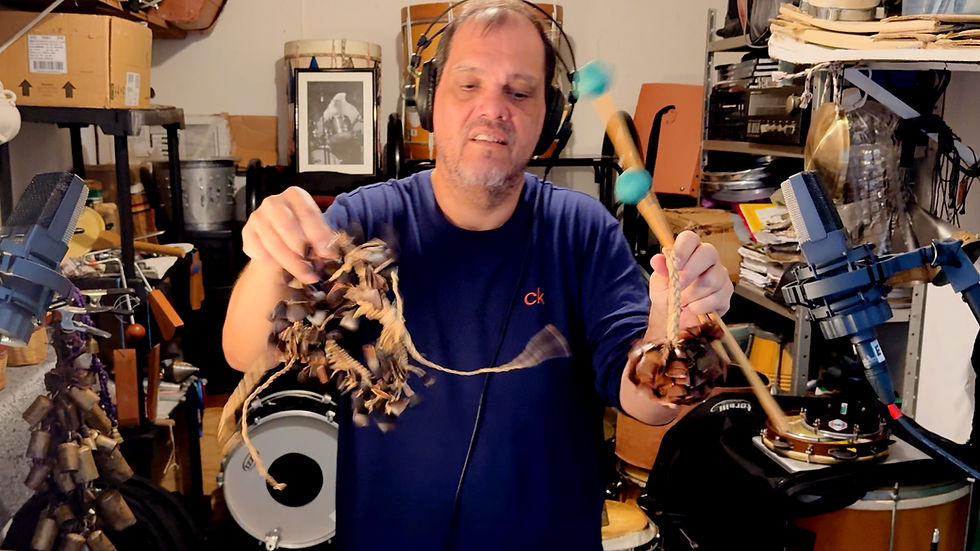 Vinícius Barros grava efeitos de percussão com sementes em seu estúdio pessoal, com diversos instrumentos ao fundo.