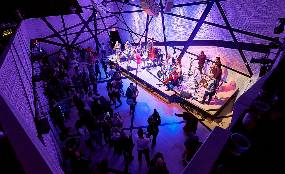 Rafael Piccolotto de Lima directing the Forró Sem Palavras orchestra at National Sawdust in Brooklyn during the Forró New York Weekend 2023, with musicians performing while the audience watches at the beginning of the show.