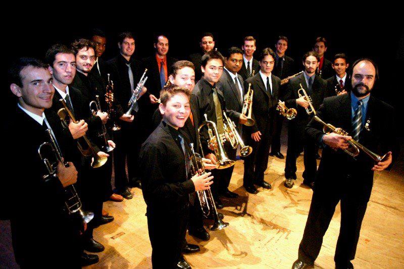 Integrantes da Oficina Trompetando posando com trajes formais de concerto no auditório da UNICAMP no início dos anos 2000, com o professor e diretor Clovis Beltrami à direita.