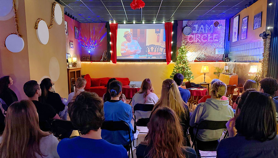 Participants sit facing a projection screen to watch documentary material about Luiz Gonzaga during the celebration in The Hague.