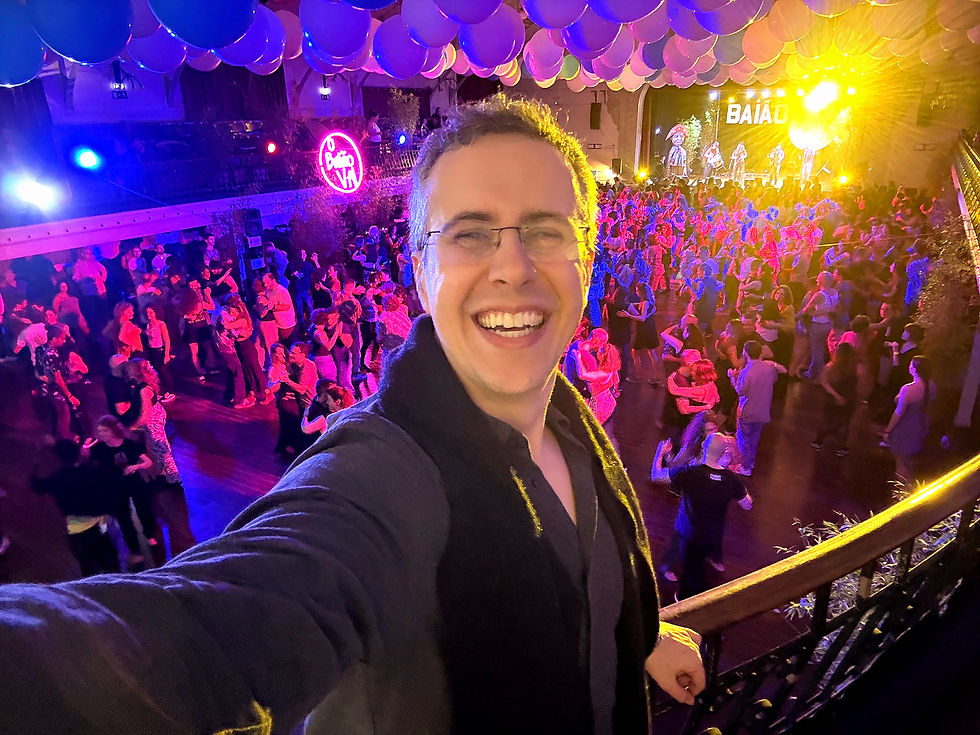 Selfie of Rafael Piccolotto de Lima at the Baião Vai forró festival in Lisbon, taken from a balcony at Voz do Operário, showing a crowded dance floor and live band performing below.