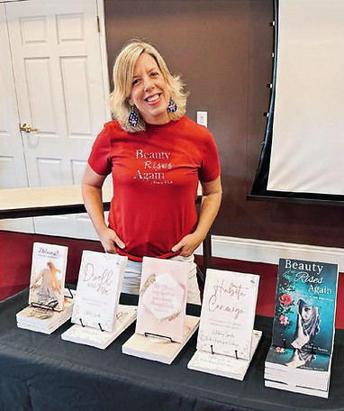 Whitney Sparks speaking at McMillan Memorial Library in Overton, TX. Devotional book on the table include Delivered! Finding Hope in the Storms of Life, Dwell with Me: Growing in Your Spiritual Walk with Jesus, a journal, Habita Conmigo, and Beauty Rises Again: From Brokenness to New Beginnings.