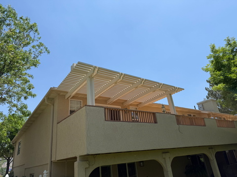 Beige house with pergola on the top under a bright blue sky.
