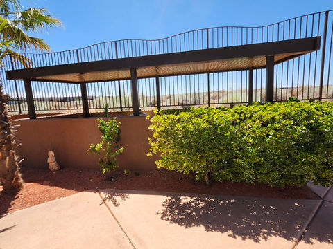Patio pergola with black fence and green bushes against a blue sky.