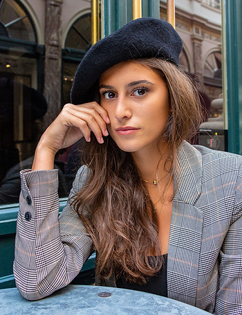 Portrait d'une jeune femme à la table d'un café à Bruxelles. Elle porte un béret et son menton repose sur sa main. 