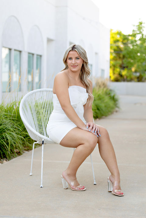 Piedmont High School Senior girl wearing a white dress sitting on a white chair in the Paseo Arts District in Downtown Oklahoma City