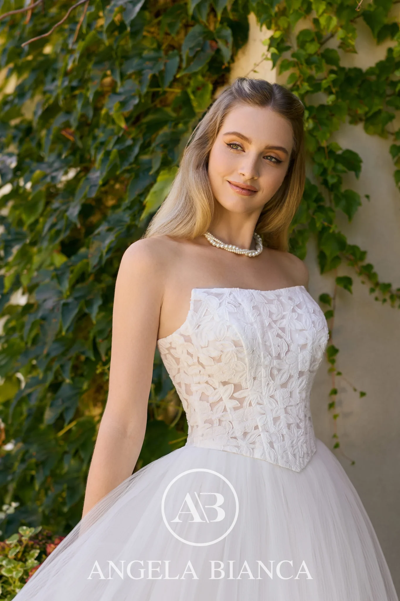 close up of a model posing in an ivory weddign dress. We can see a strapless square basque bodice and tulle skirt.