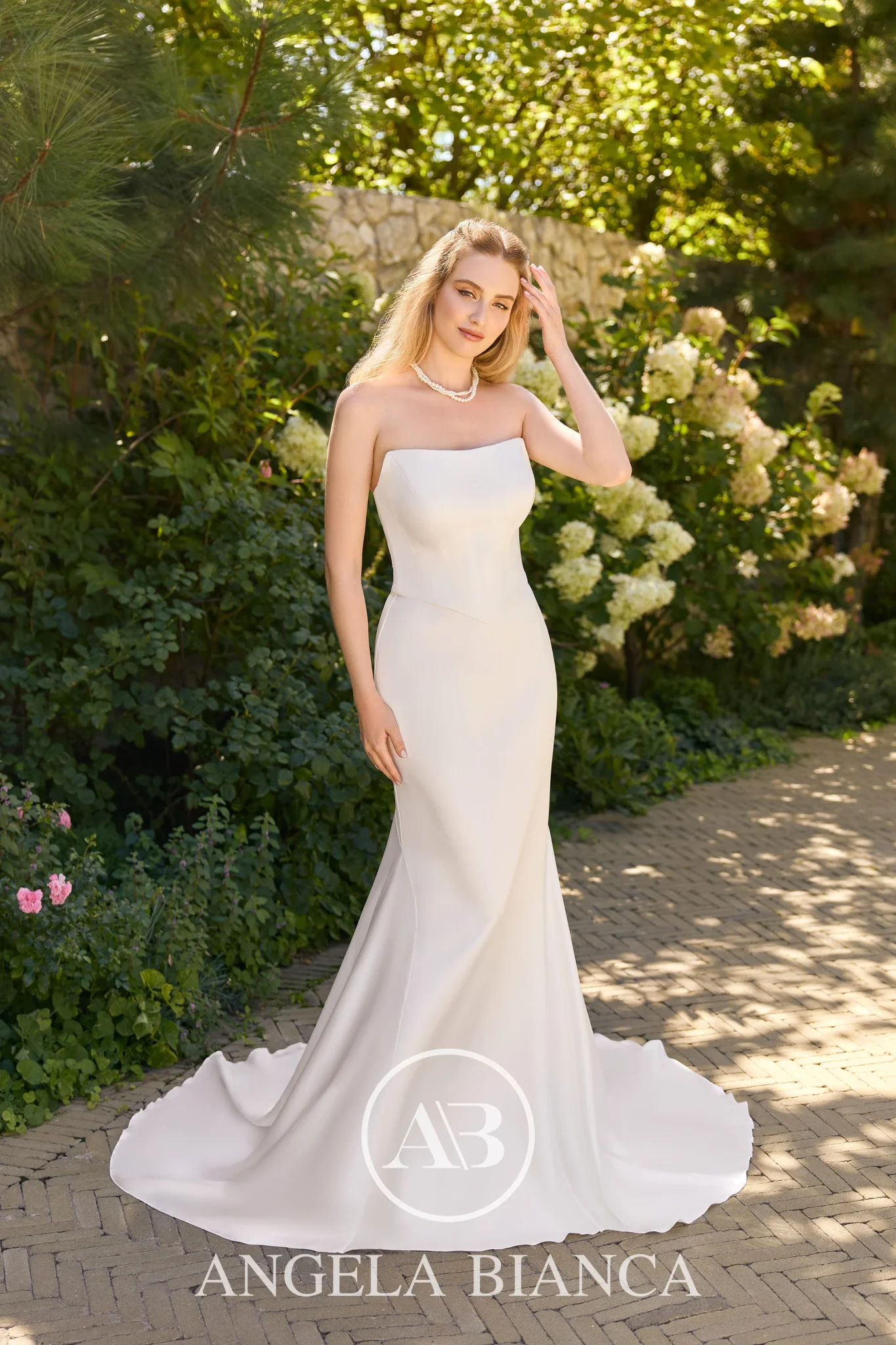 Model poses in a strapless fitted Ivory wedding dress. The dress is elegantly plain making a feature of clean lines and no detail.
