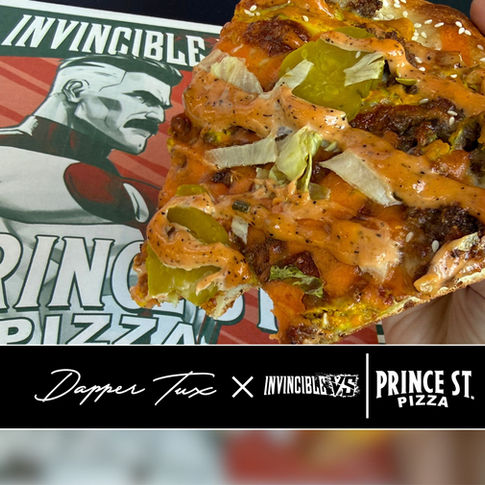 Hand holds a saucy pizza slice with pickles and lettuce over an Invincible/Prince St. Pizza menu.