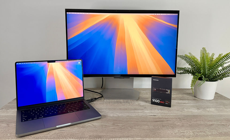Laptop and monitor with vibrant orange-blue screens on a wooden desk, alongside a Samsung 9100 PRO SSD box and a potted fern.