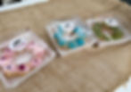 Three colorful doughnuts in plastic boxes, labeled "Forza Horizon 6," on a burlap surface. Pink, blue, and green icing visible.