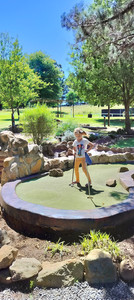 Child playing putt putt with trees in background