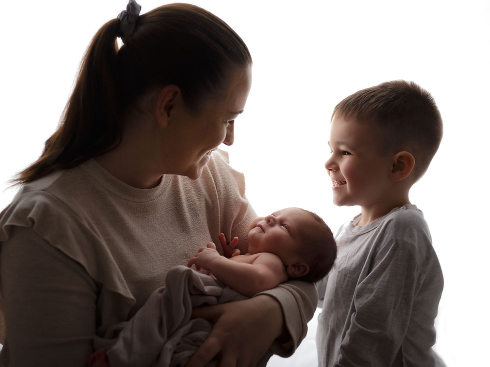 Mother and son smiling at a newborn in studio family photography.