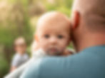 Baby looking over father's shoulder during outdoor session.