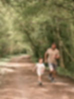 A father and son running on an outdoor forest trail.