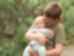 Young boy holding a baby by an outdoor family photographer