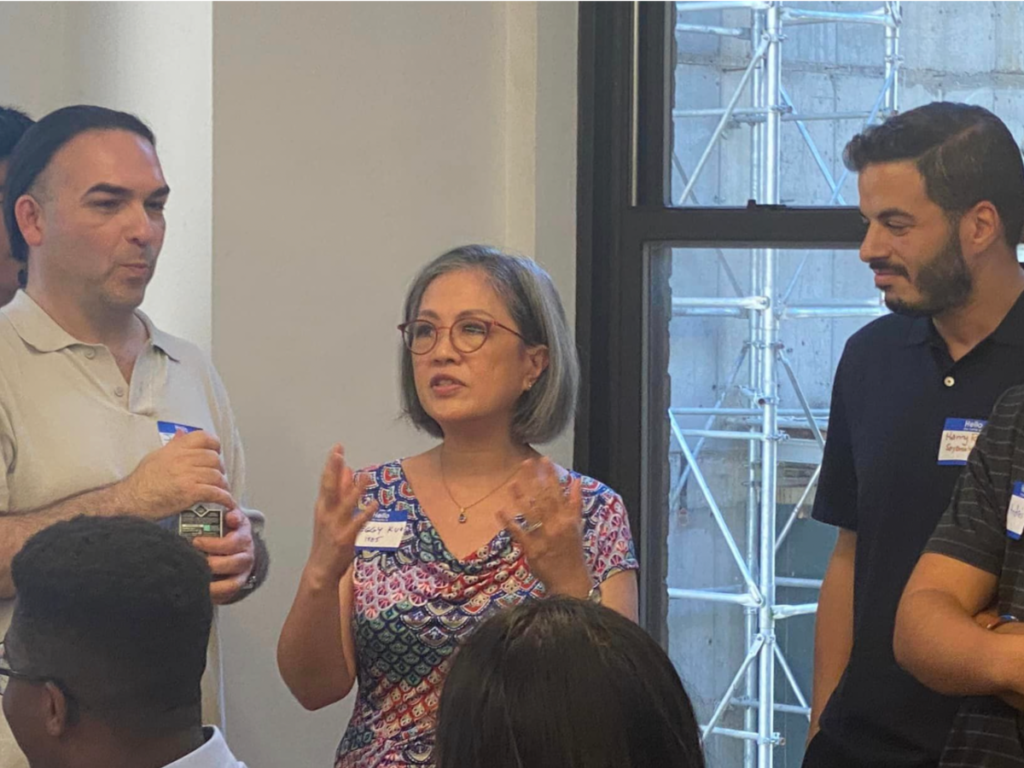 An alum who is gesturing and speaking stands between two other alums