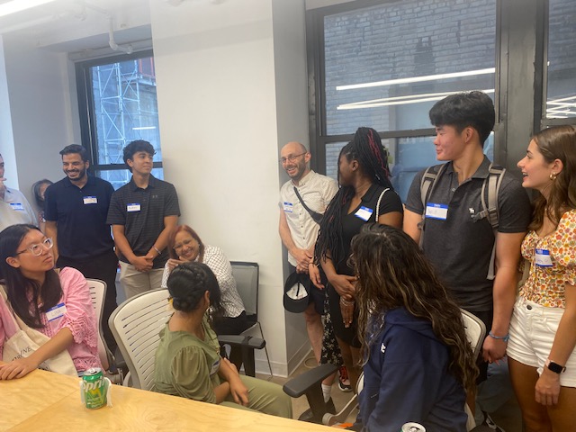 Students and alums stand or sit around a table and mingle