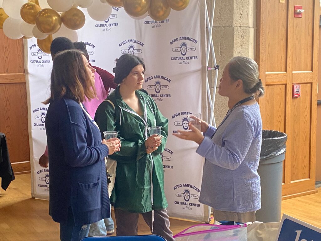 Three people stand holding drinks and talking