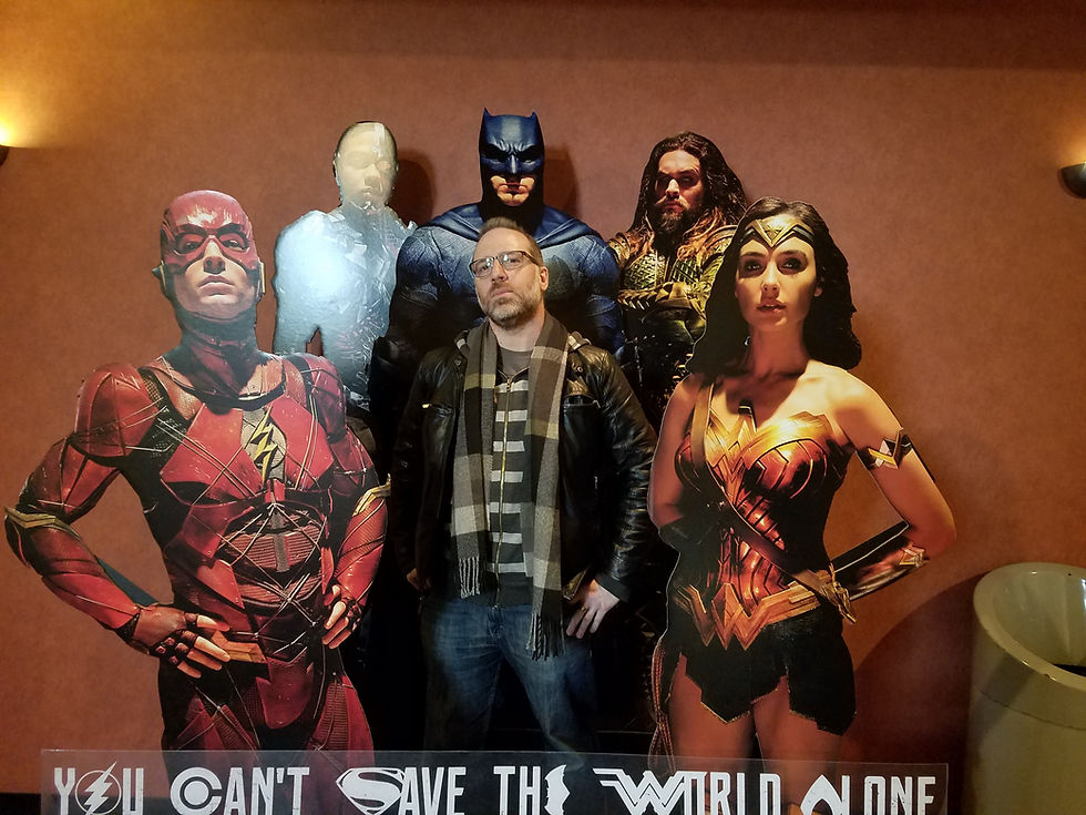 Professional voice actor Tom Dheere posing with Justice League cardboard cutouts at a movie theater in 2017.
