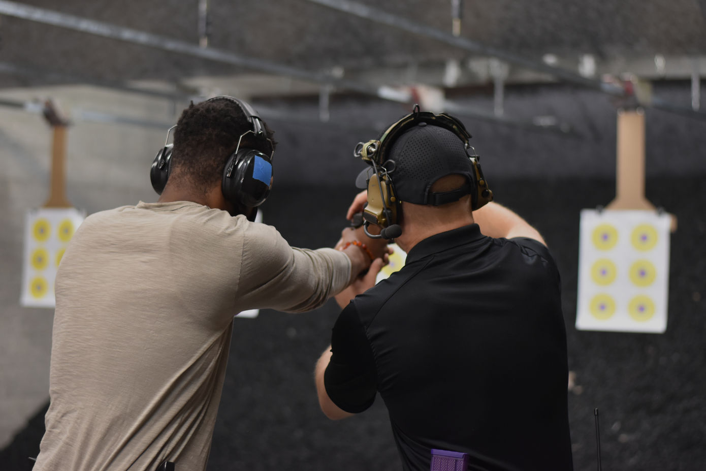 Two men practice shooting handguns, targets and hearing protection at range.