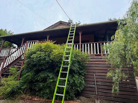 Green ladder leaning against a house roof to repair electrical fault