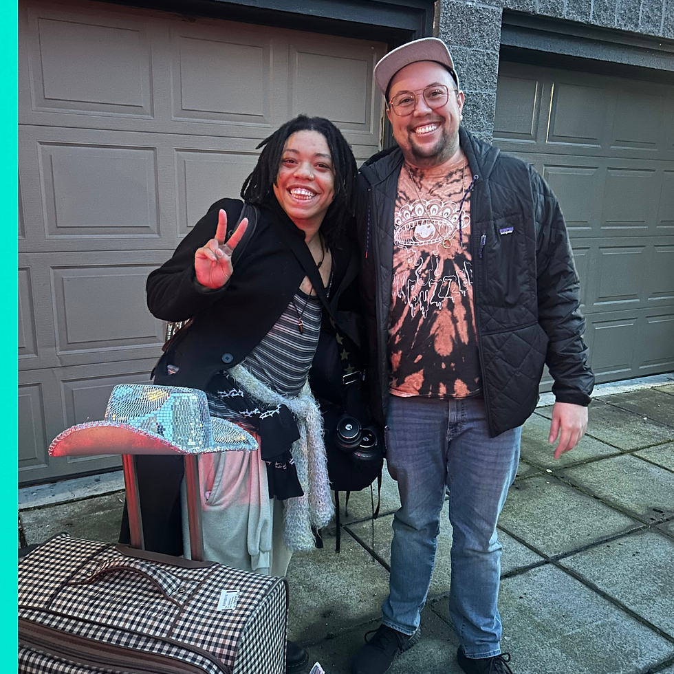 2 people smiling, one of them is holding up a peace sign with their fingers.