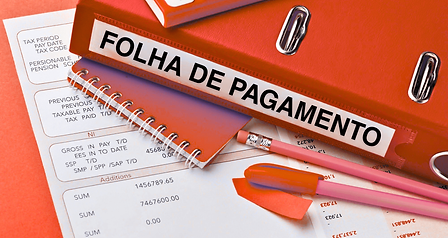 Um pasta vermelha coom uma etiqueta onde está escrito "folha de pagamento" enquanto uma folha de pagamento está embaixo da pasta e um lápis, uma caneta e um bloco de notas estão espalhados na mesa.
