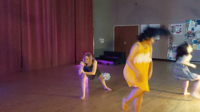 Gif: Women in colorful dresses frantically dancing in a studio lit pink and blue. Think Pina Bausch.