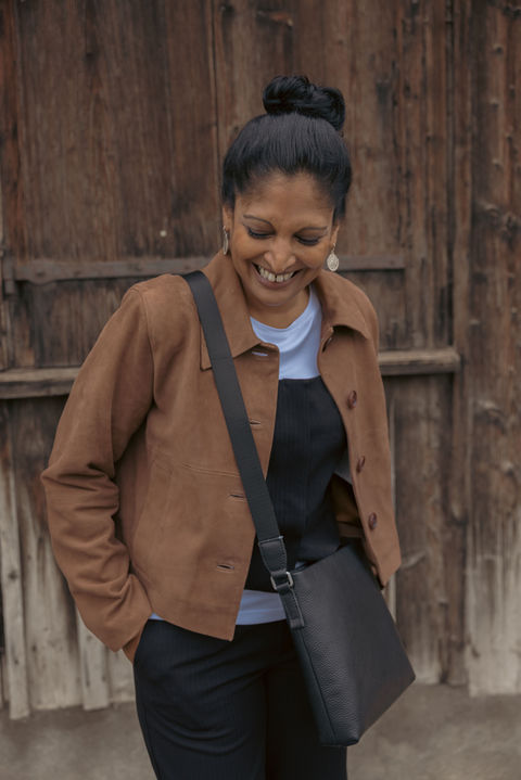 Junge Frau lachend, mit brauner Velour Lederjacke und schwarzer Umhängetasche