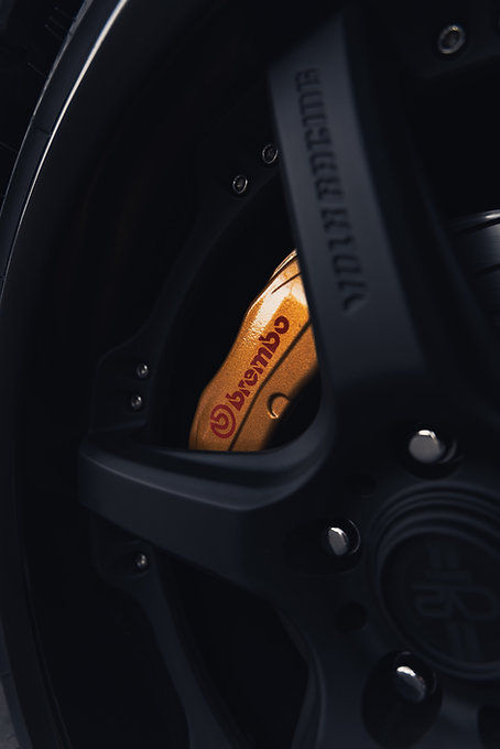 Transparenter Aufkleber mit roter Brembo Schrift und Brembo Logo auf Bremssattel hinter schwarzer Felge.