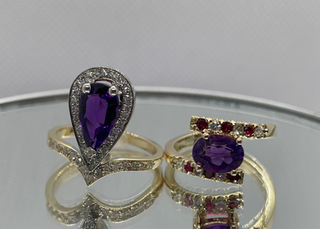 Two luxury handmade rings from Marchioness Jewelry Boutique — oval Brazilian amethyst ring in 14K yellow gold with diamonds and rubies (Fleur d’Améthyste) next to pear-cut Brazilian amethyst ring in 14K white and yellow gold with diamond pavé (Pear Améthyste) — Custom Jewelry Toronto.