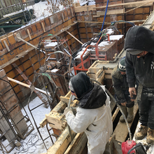 Workers pouring reinforced concrete into commercial foundation forms at a construction site.