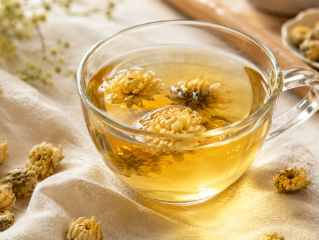 A clear glass cup of golden chrysanthemum tea with dried chrysanthemum flowers