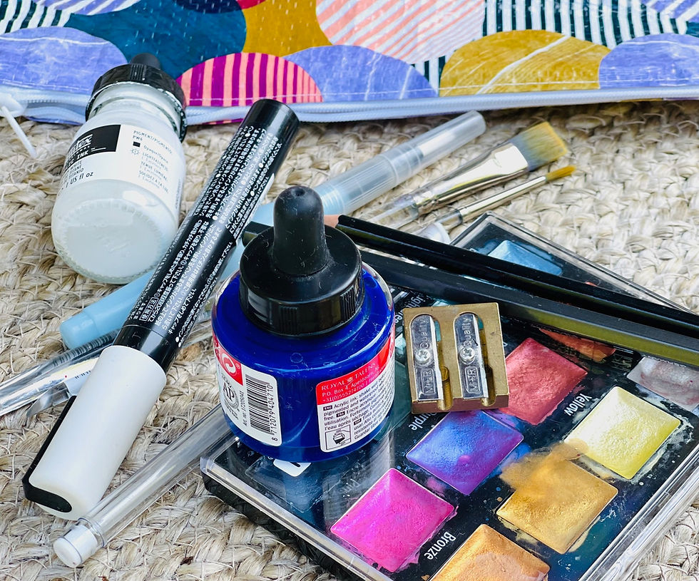 A flat lay of mixed media art supplies for travel, including watercolor paints, brushes, markers, ink, and a journal pouch.