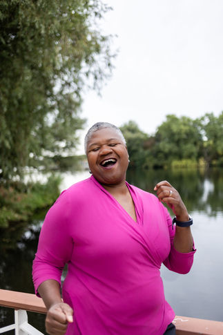 portrait photographer Brighton black woman short hair pink top dancing by lake