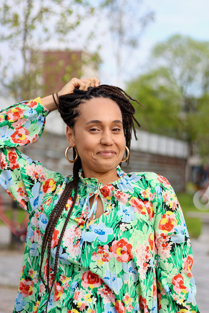 Woman in floral dress holds hair braids and laughs to camera