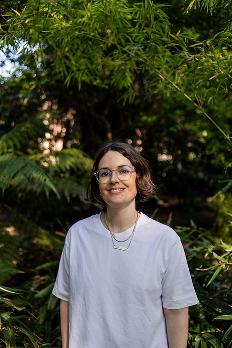 headshots Brighton woman with white tshirt and glasses in front of foliage in the late afernoon sun